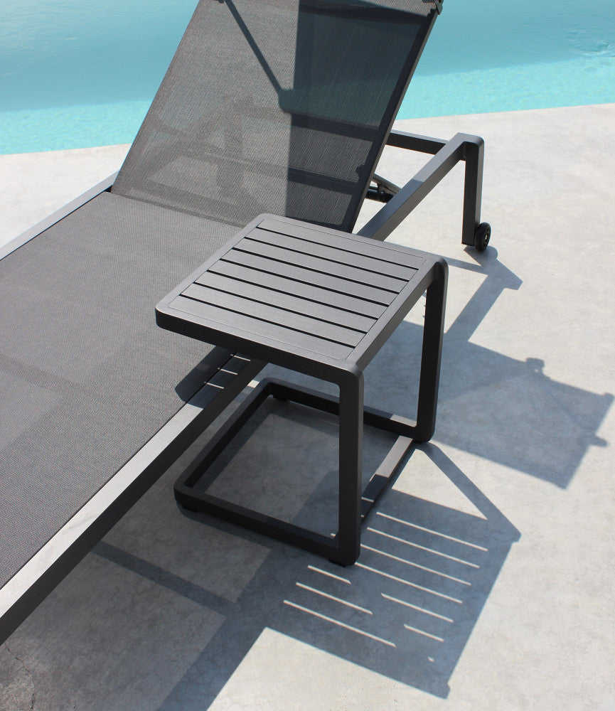 Tavolino Alimos in alluminio antracite affiancato a un lettino prendisole a bordo piscina.