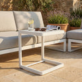 Tavolino da giardino Alimos in alluminio bianco affiancato a un divano outdoor con bicchiere d'acqua