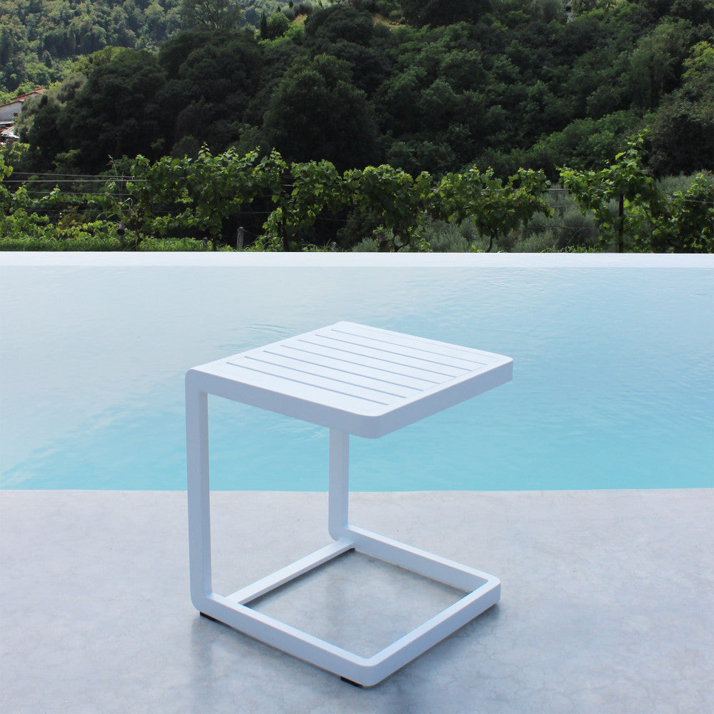 Tavolino minimalista in alluminio bianco a bordo piscina, riflessi di luce naturale