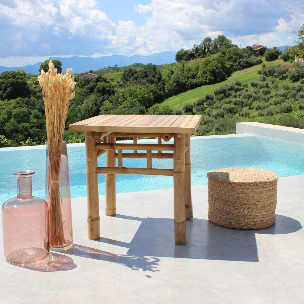 Angolazione laterale del tavolino in legno a bordo piscina, che evidenzia i dettagli dei giunti e la superficie a doghe.