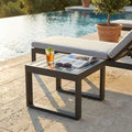 Tavolino da giardino Cuba in alluminio antracite a bordo piscina con drink e rivista.