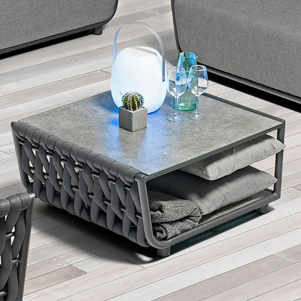 Primo piano del tavolino Galapagos illuminato da una lampada da tavolo, che mostra la texture del textilene e i cuscini riposti nel vano inferiore.