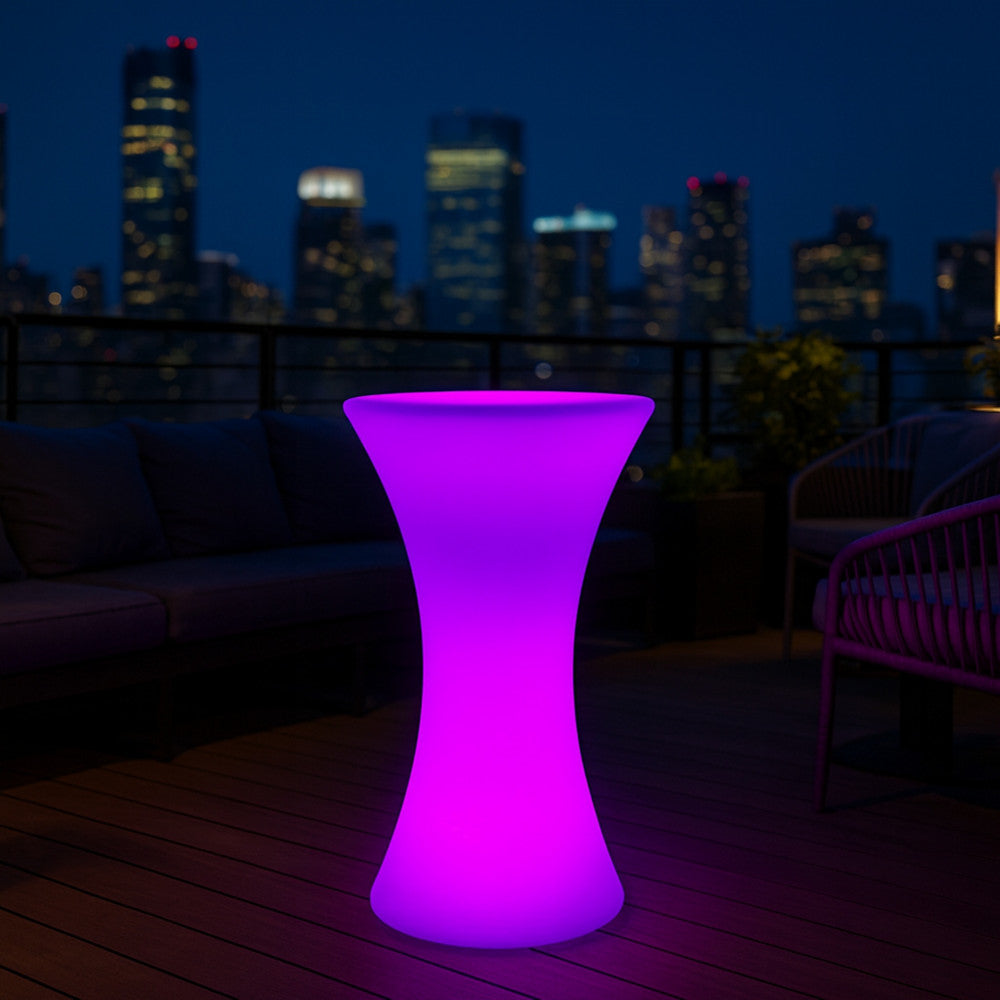 Tavolino luminoso Perseus in polietilene rosa che illumina un elegante rooftop urbano di notte.
