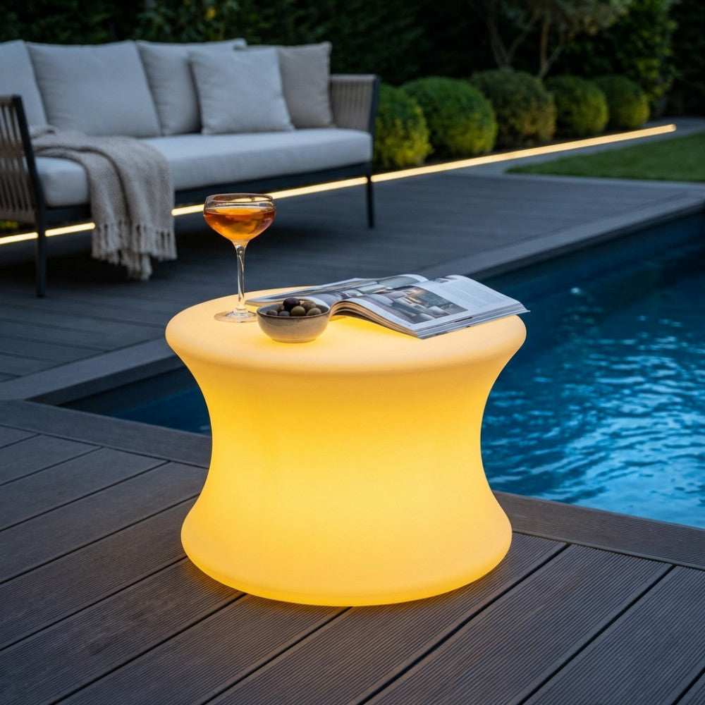 Tavolino luminoso Pegasus in polietilene giallo a bordo piscina durante il giorno, con un drink e una rivista.