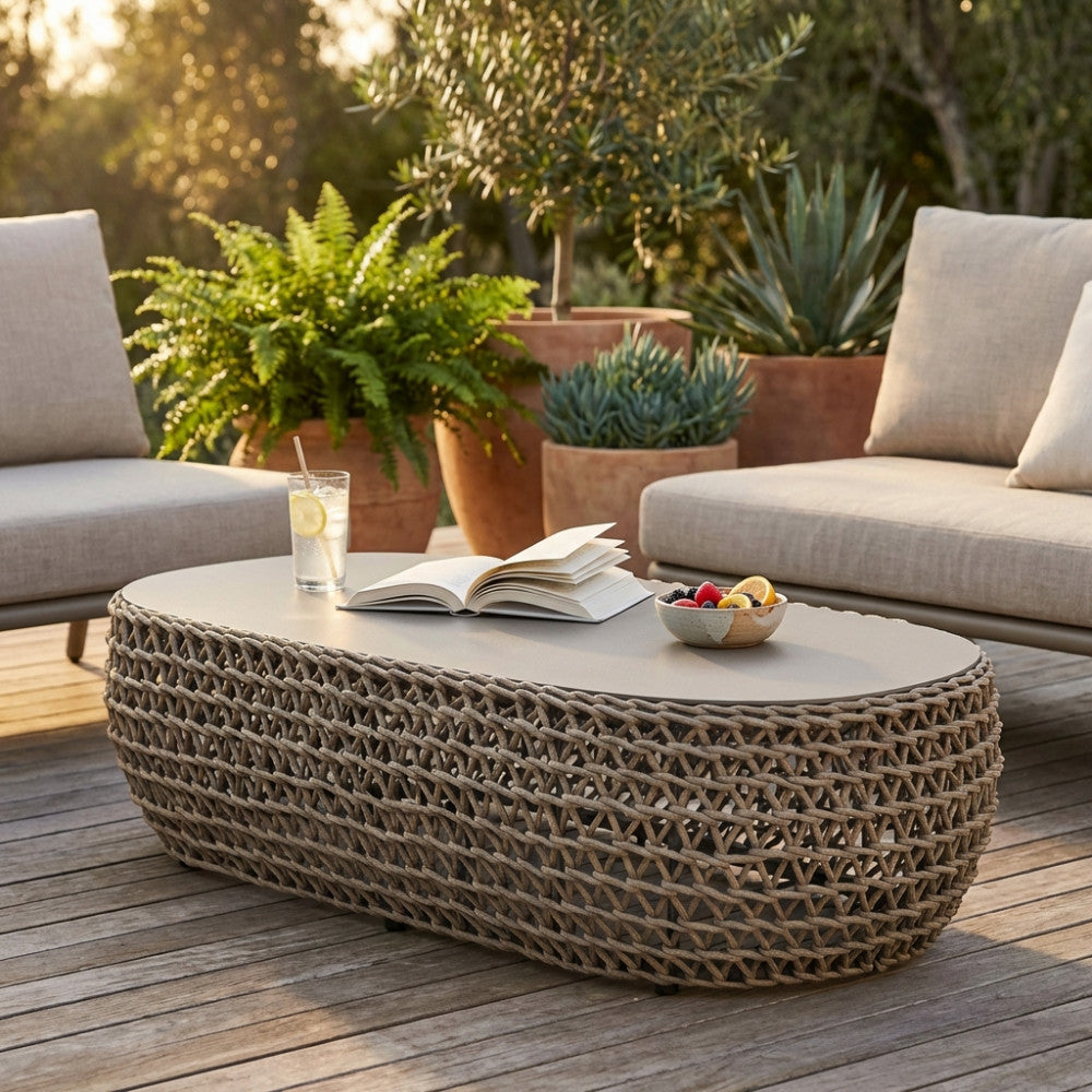 Tavolino ovale Lafayette in corda intrecciata e alluminio, allestito su un patio in legno con libri e frutta, illuminato dalla luce del tramonto.