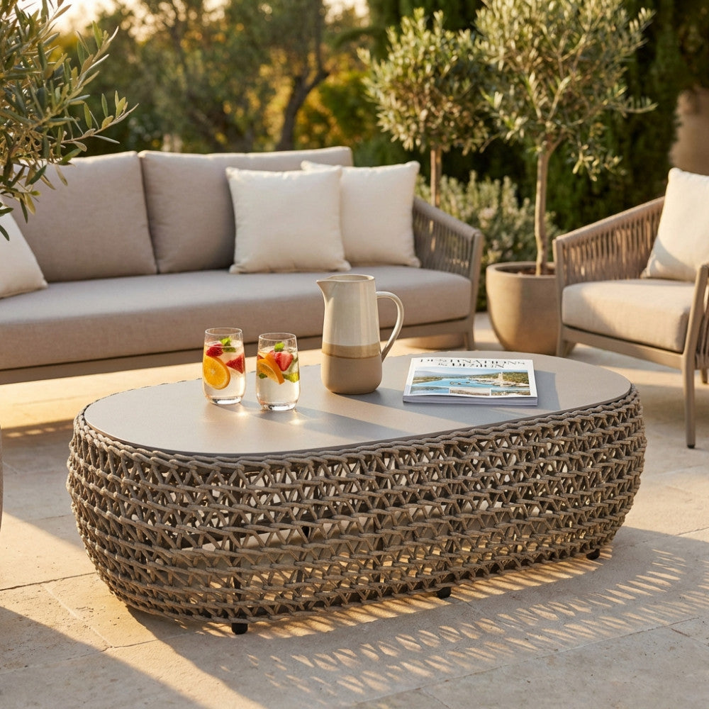 Tavolino da salotto outdoor Lafayette in corda beige, posizionato su una pavimentazione in pietra accanto a divani eleganti e bevande rinfrescanti.