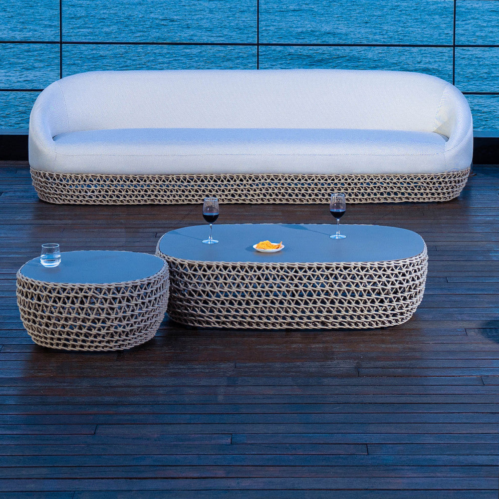 Set lounge serale con il tavolino ovale Lafayette e un tavolino rotondo abbinato, disposti su un ponte in legno scuro vicino all'acqua.