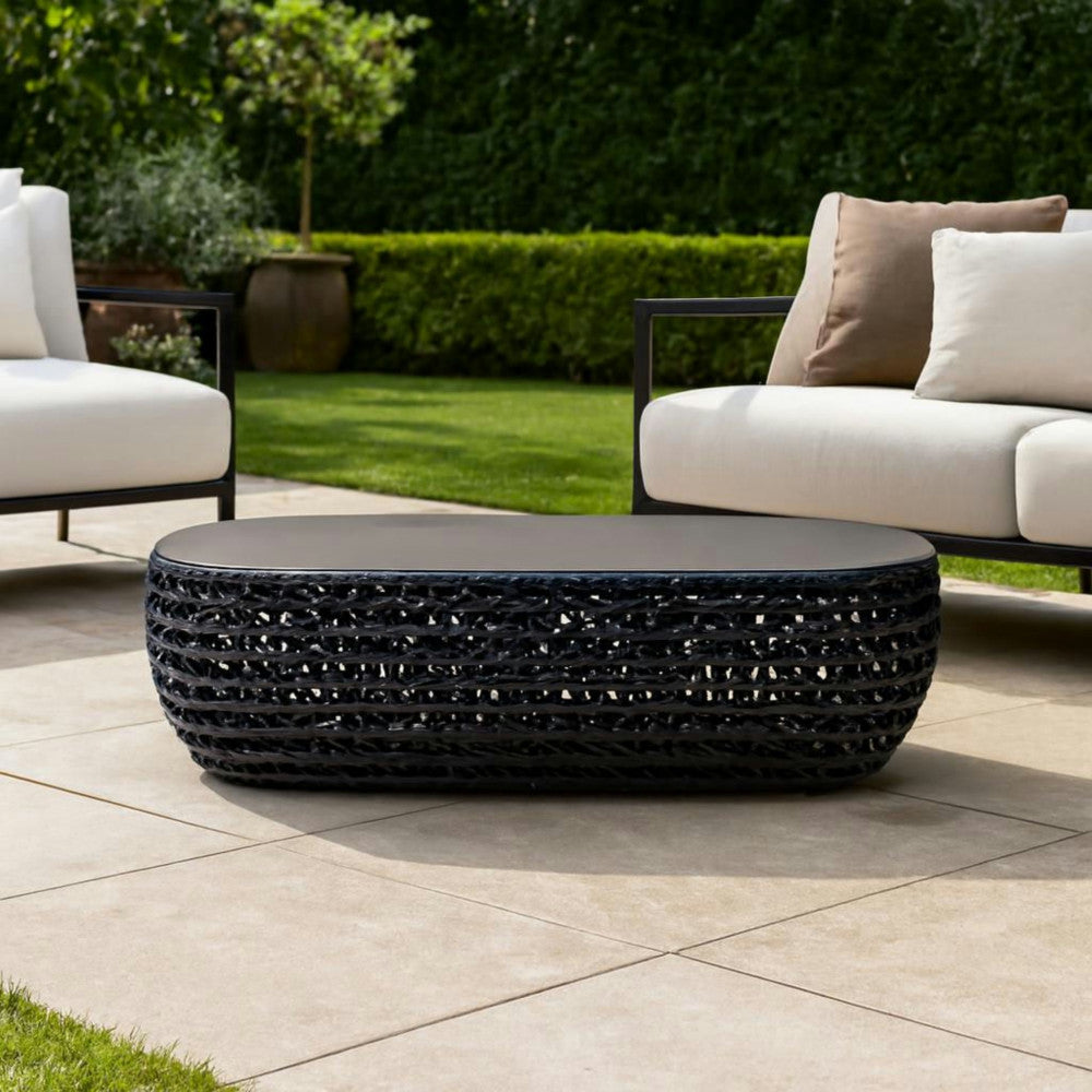 Tavolino Lafayette posizionato su una pavimentazione in pietra in un giardino verdeggiante, tra due poltrone outdoor bianche dal design moderno.