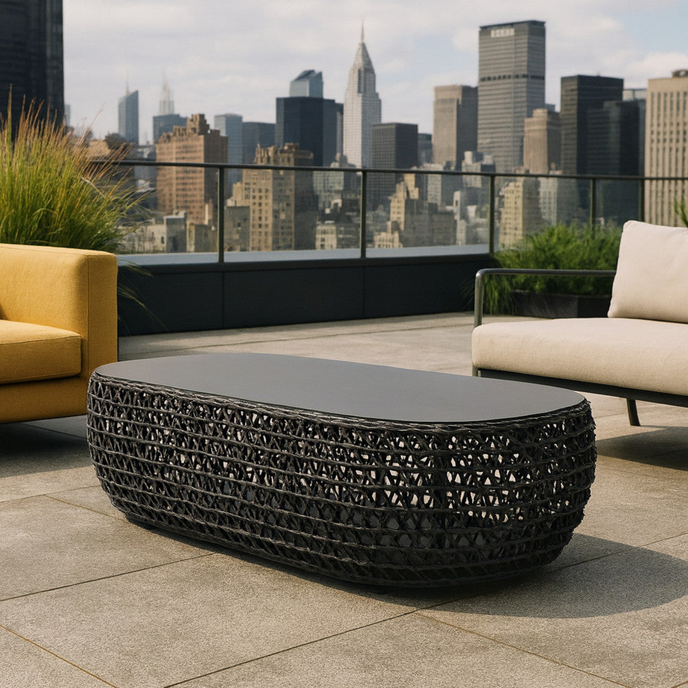 Terrazza panoramica urbana con il tavolino Lafayette in corda intrecciata, accostato a un divano giallo senape e una poltrona neutra con vista sui grattacieli.