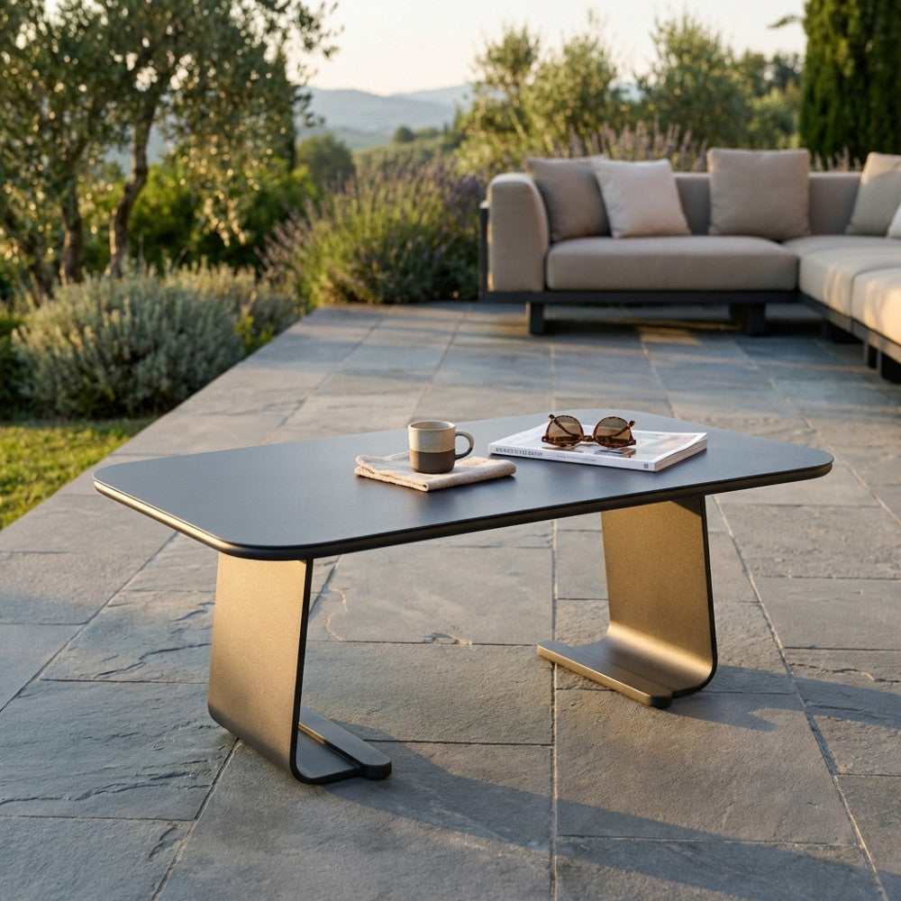 Tavolino ovale Vancouver in alluminio grigio antracite allestito su un patio in pietra al tramonto con tazza e rivista.