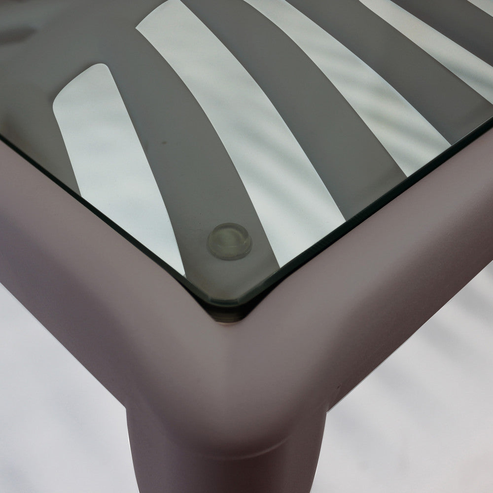 Primo piano dell'angolo del tavolino, che mostra il piano in vetro temperato appoggiato sui supporti in gomma della struttura taupe.