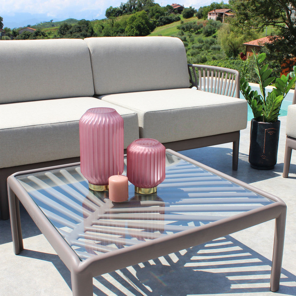 Tavolino Guaranà allestito con vasi decorativi in vetro rosa e candele, situato su una terrazza soleggiata con vista panoramica.