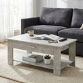 Tavolino da salotto Myrto effetto cemento ambientato davanti a un divano grigio scuro con libri e accessori.