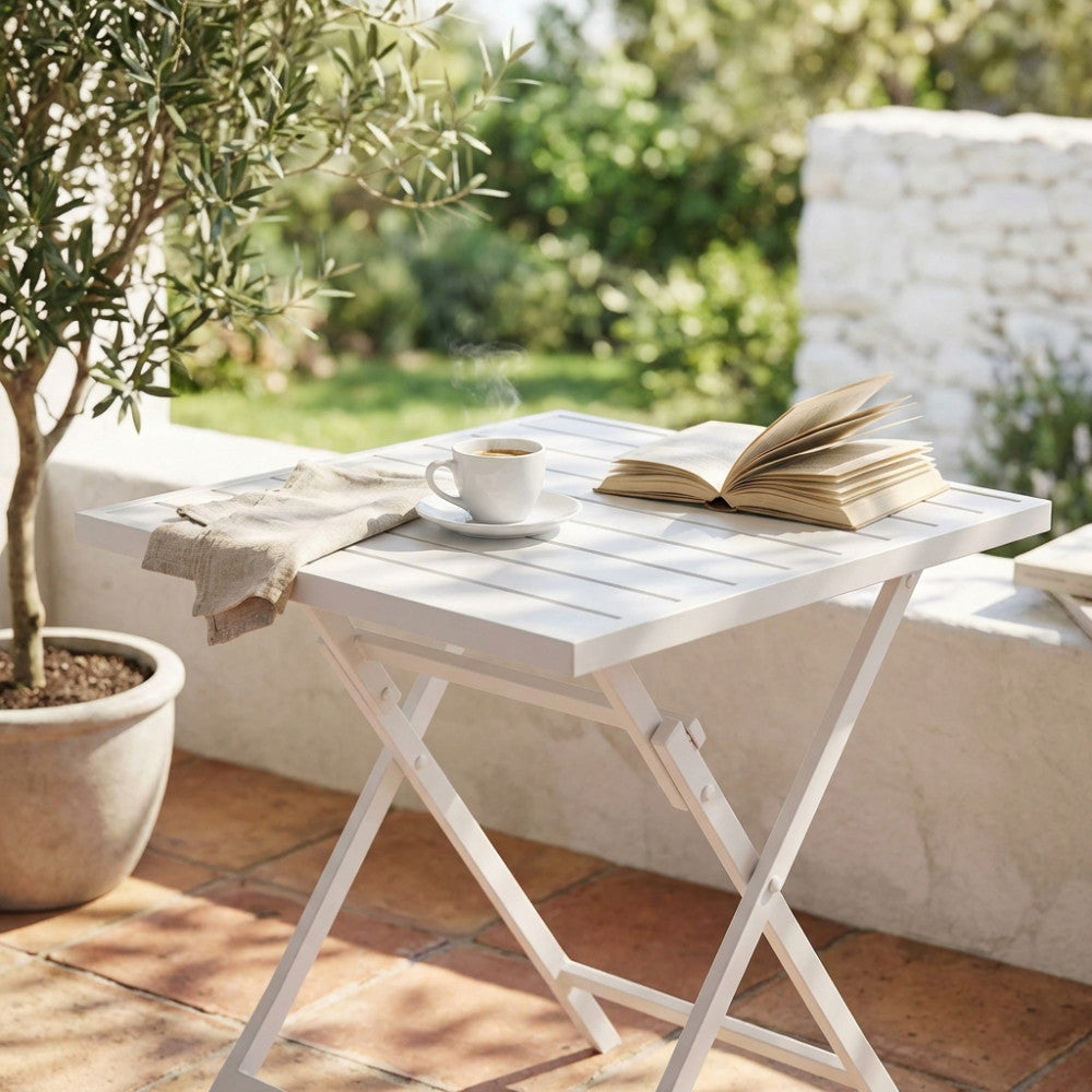 Dettaglio del tavolo pieghevole Alabama con una tazza di caffè e un libro aperto, immerso nella luce naturale del giardino.