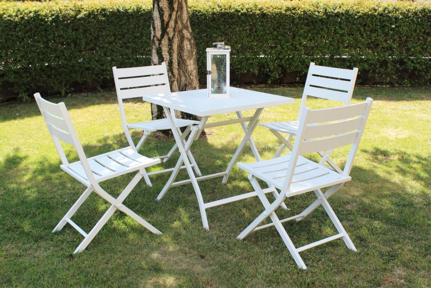 Set completo da esterno con il tavolo Alabama e quattro sedie pieghevoli abbinate, disposti su un prato verde all'ombra di un albero.