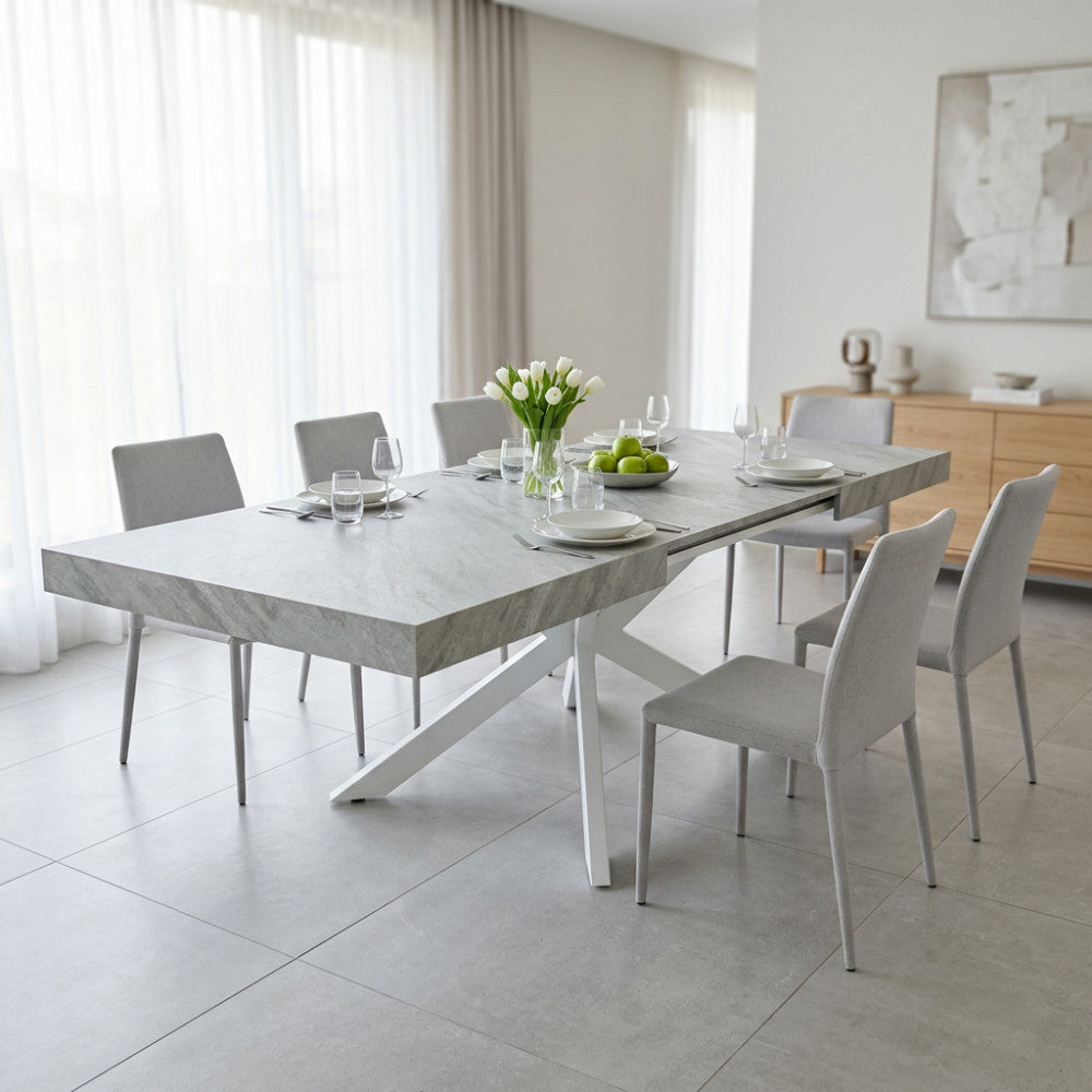 Tavolo allungabile Darren in melaminico effetto pietra grigio ambientato in una sala da pranzo luminosa con sedie grigie.