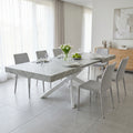 Tavolo allungabile Darren in melaminico effetto pietra grigio ambientato in una sala da pranzo luminosa con sedie grigie.