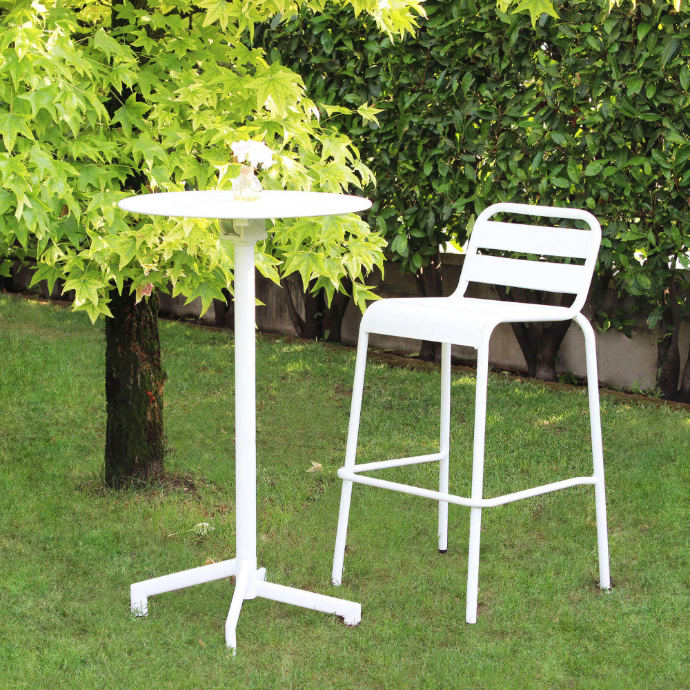 Tavolo alto VEGA Ø 60 in acciaio bianco abbinato a uno sgabello in metallo in un giardino verdeggiante.