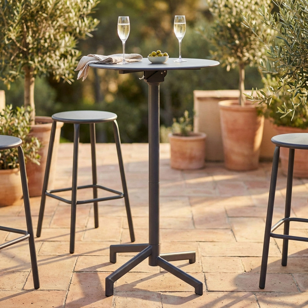 Tavolo alto da giardino in acciaio grigio scuro allestito con calici su una terrazza in cotto.