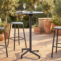 Tavolo alto da giardino in acciaio grigio scuro allestito con calici su una terrazza in cotto.