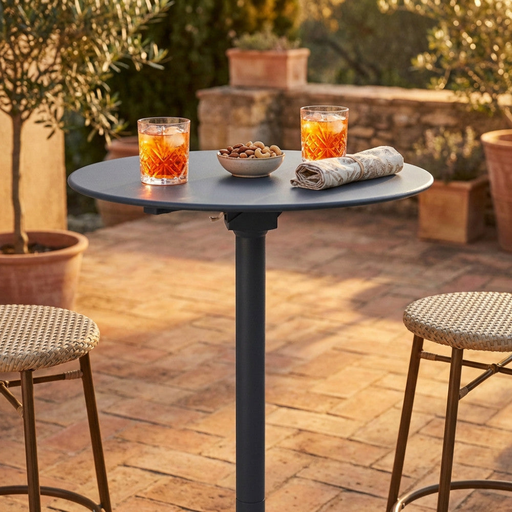 Dettaglio del piano rotondo del tavolo alto in acciaio con cocktail e stuzzichini alla luce del tramonto.