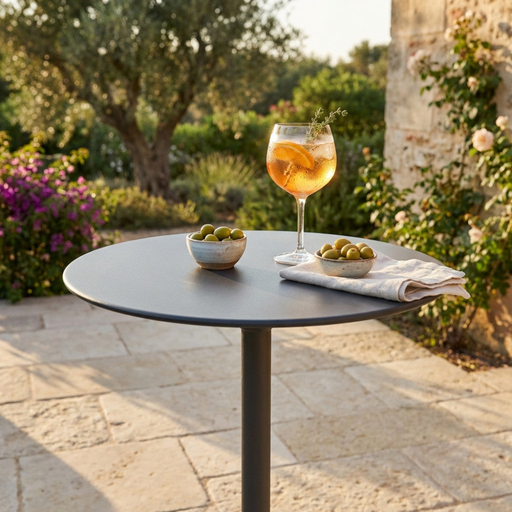 Dettaglio del piano rotondo del tavolo Vega Ø 60 con cocktail e olive in un giardino soleggiato.