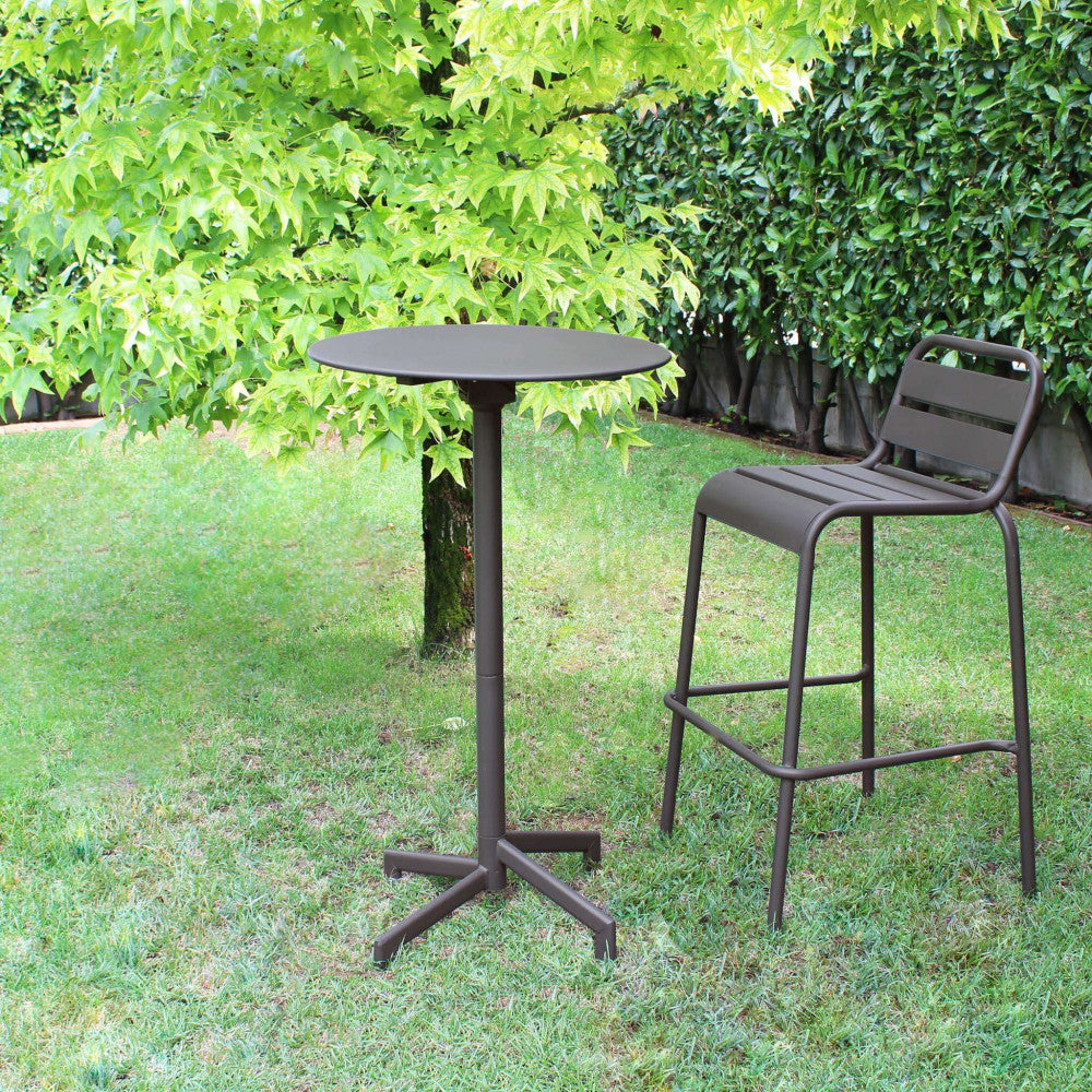 Tavolo alto Vega ambientato in un giardino verde, abbinato a uno sgabello in metallo coordinato.