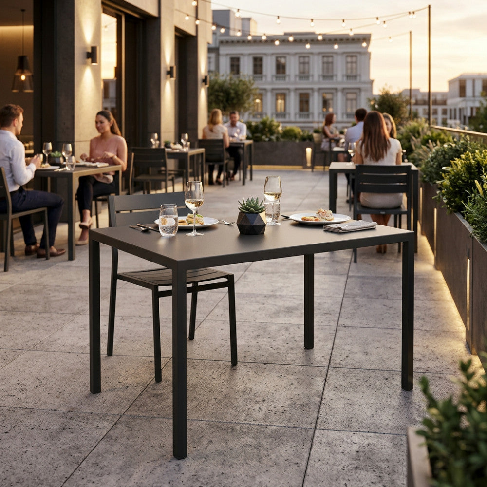 Tavolo da giardino in metallo antracite allestito per una cena elegante su una terrazza al tramonto.