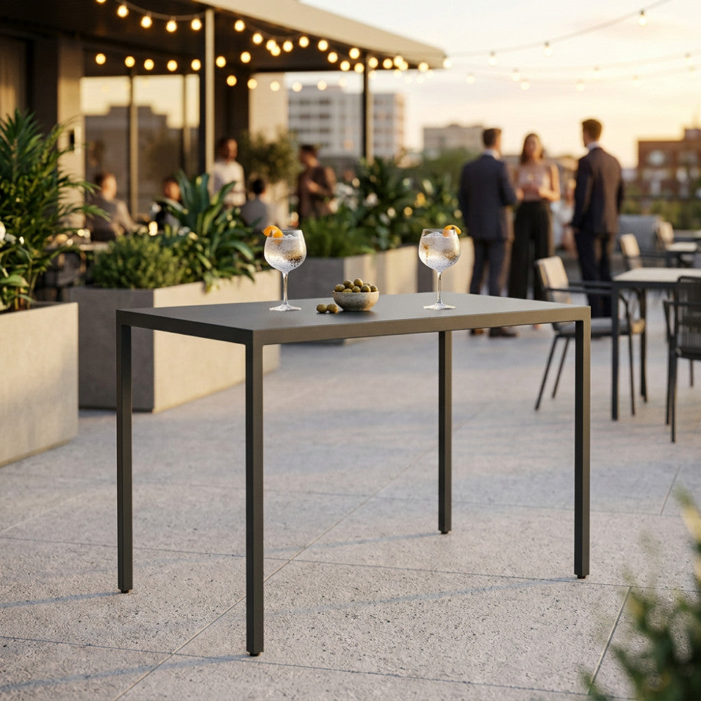 Tavolo alto in metallo antracite allestito con due cocktail e olive su una terrazza elegante al tramonto.