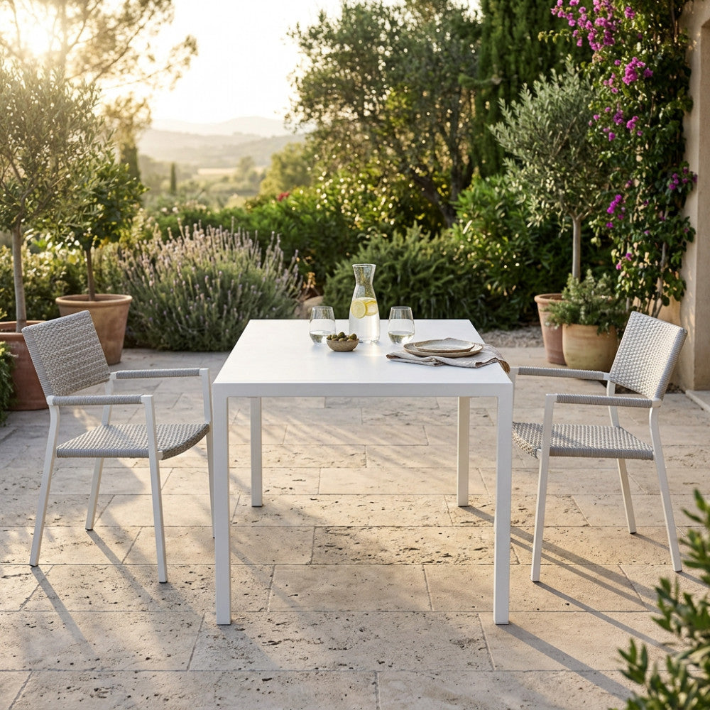 Tavolo da giardino in acciaio bianco allestito per un aperitivo all'aperto su una terrazza in pietra.