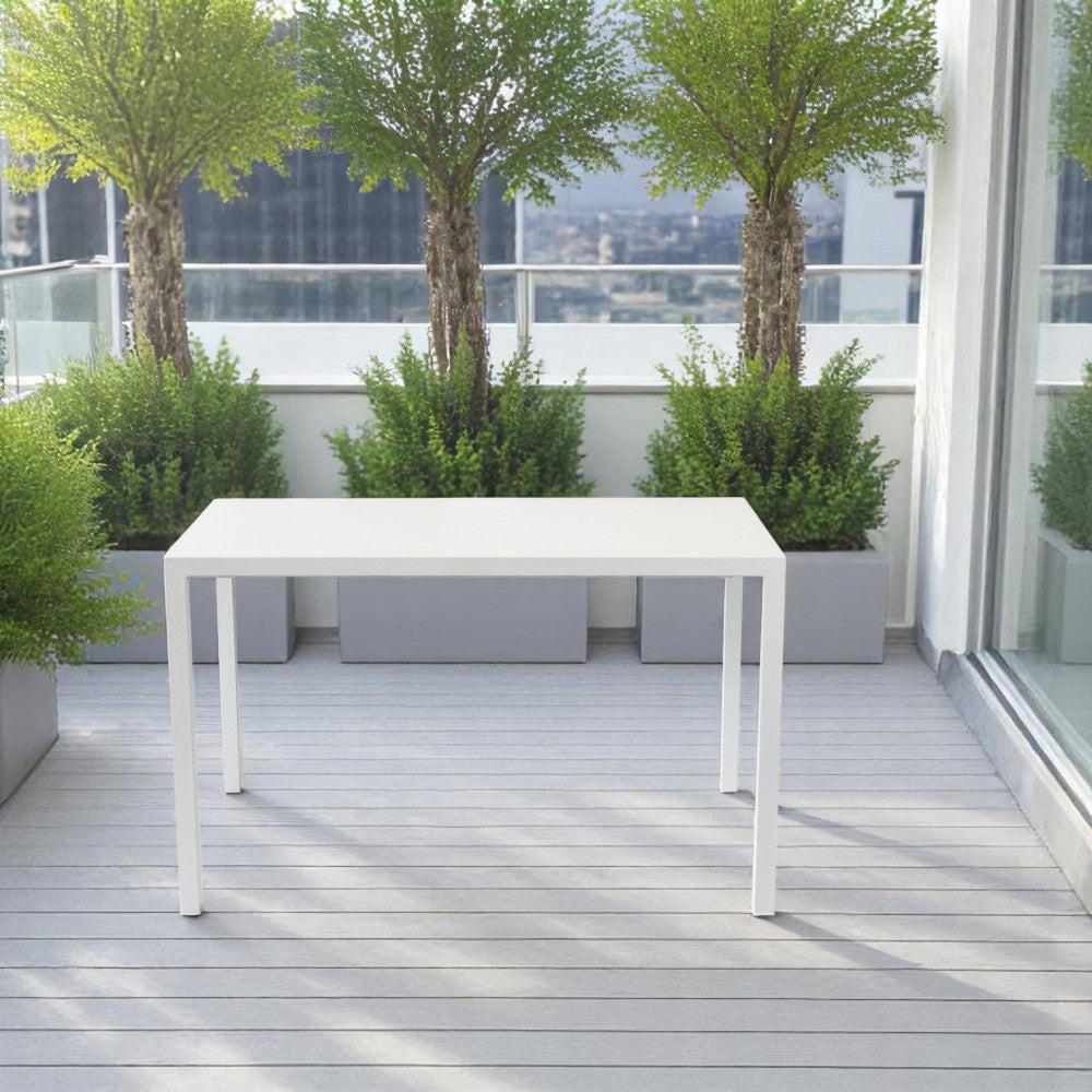 Tavolo moderno in acciaio bianco posizionato su un balcone in legno con piante decorative sullo sfondo.