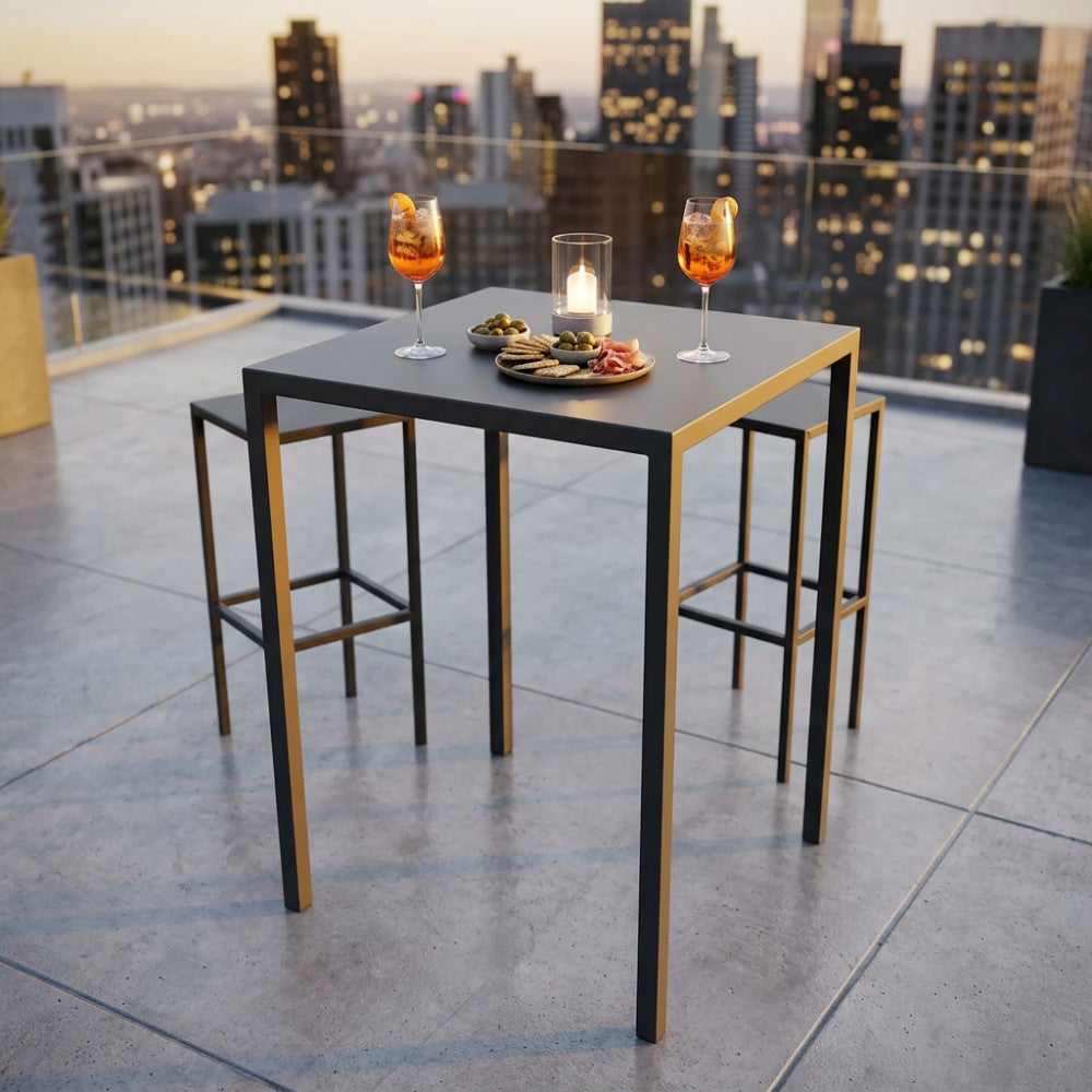 Tavolo alto quadrato in metallo antracite su una terrazza panoramica al tramonto, allestito con drink e stuzzichini, affiancato da due sgabelli minimalisti.