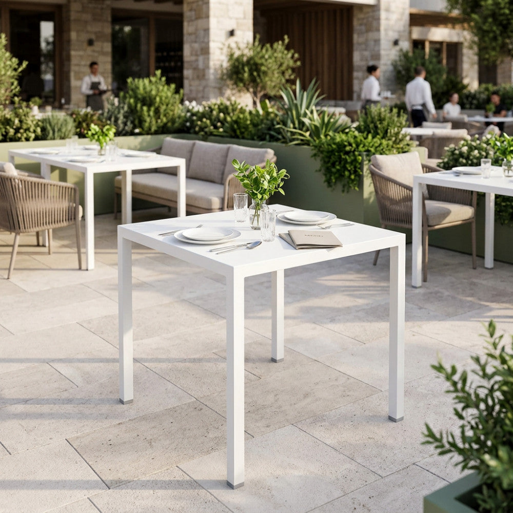 Un tavolo da giardino in metallo bianco autolivellante, apparecchiato per il pranzo in un lussuoso patio esterno soleggiato.