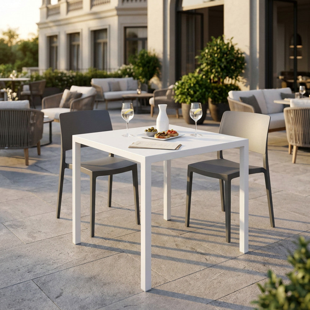 Il moderno tavolo da esterno quadrato bianco abbinato a eleganti sedie grigie, allestito con bevande e stuzzichini su una terrazza in pietra.