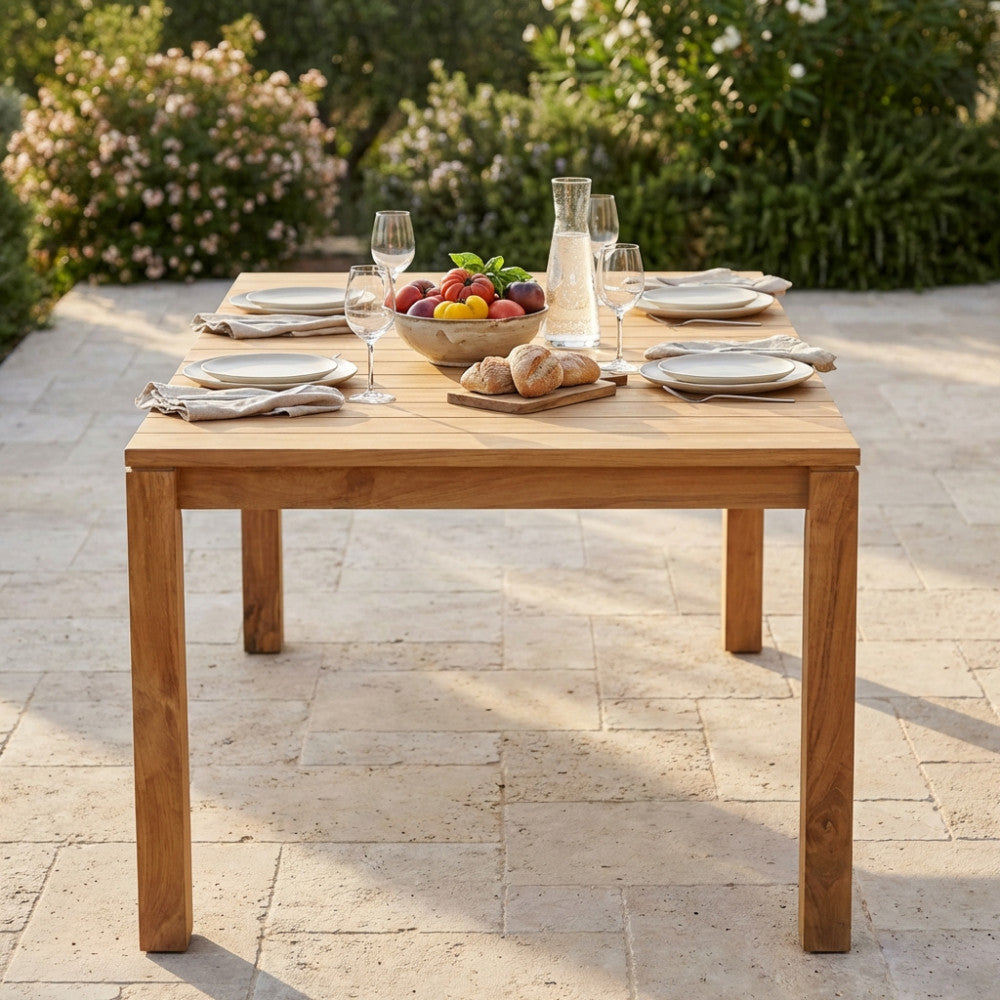 Dettaglio del piano a doghe del tavolo da giardino in teak Bandung con mise en place elegante e luce naturale.
