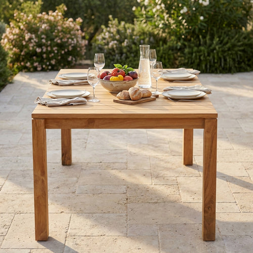 Dettaglio del piano a doghe del tavolo da giardino in teak Bandung con mise en place elegante e luce naturale.