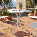 Tavolo da giardino quadrato in acciaio bianco allestito su un patio in terracotta con vista mare.