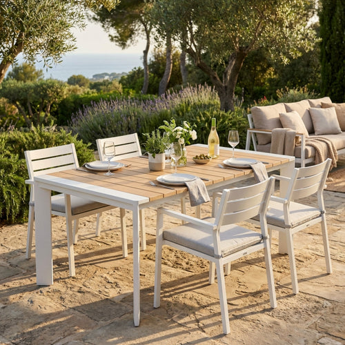 Tavolo da pranzo Brooklyn allungabile effetto legno allestito in un giardino lussuoso con sedie bianche e divani.