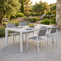 Allestimento da pranzo all'aperto con il tavolo da giardino Carson in alluminio bianco circondato da sedie grigie su un patio in pietra.
