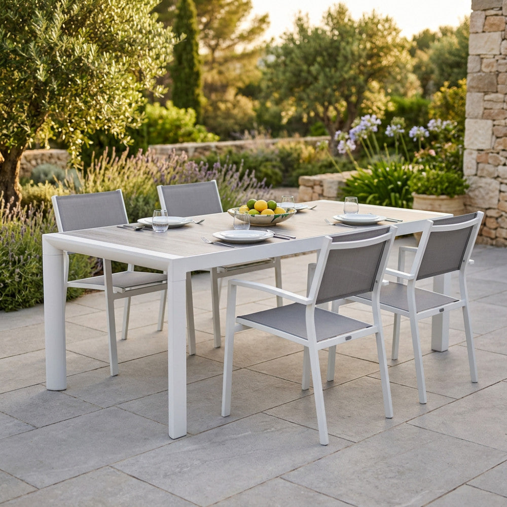 Allestimento da pranzo all'aperto con il tavolo da giardino Carson in alluminio bianco circondato da sedie grigie su un patio in pietra.