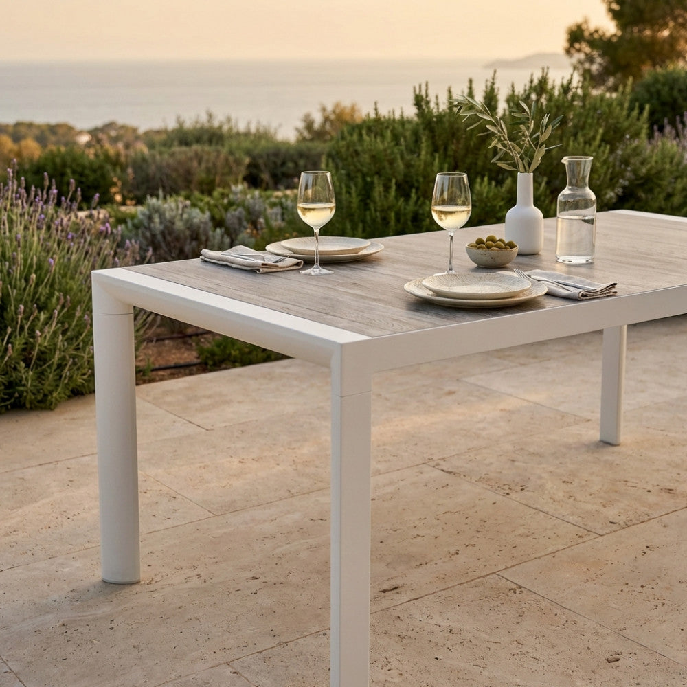 Primo piano del tavolo da giardino Carson apparecchiato con calici di vino, con vista su un suggestivo paesaggio costiero.