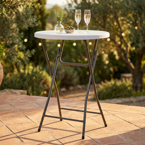 Tavolo da catering alto rotondo con piano bianco e struttura in acciaio grigio, allestito all'aperto con calici e stuzzichini su una pavimentazione in cotto.