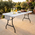 Tavolo da catering CT804530 allestito all'aperto con caraffe d'acqua, pane e frutta, illuminato dalla luce del tramonto.