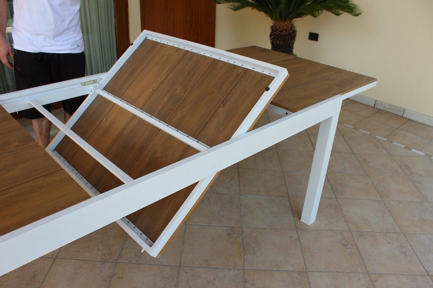 Dimostrazione dell'apertura della prolunga a ribalta in polywood marrone del tavolo.
