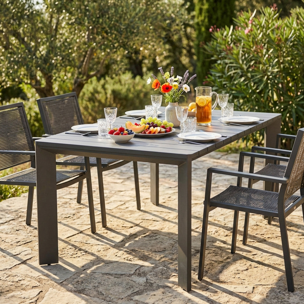 Tavolo da giardino moderno allestito per un pranzo all'aperto con sedie in corda intrecciata.