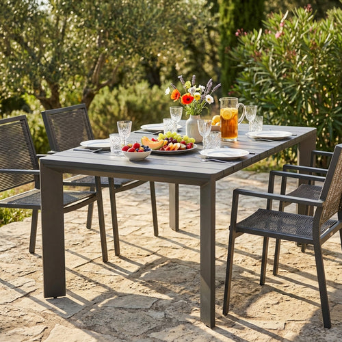 Tavolo da giardino moderno allestito per un pranzo all'aperto con sedie in corda intrecciata.