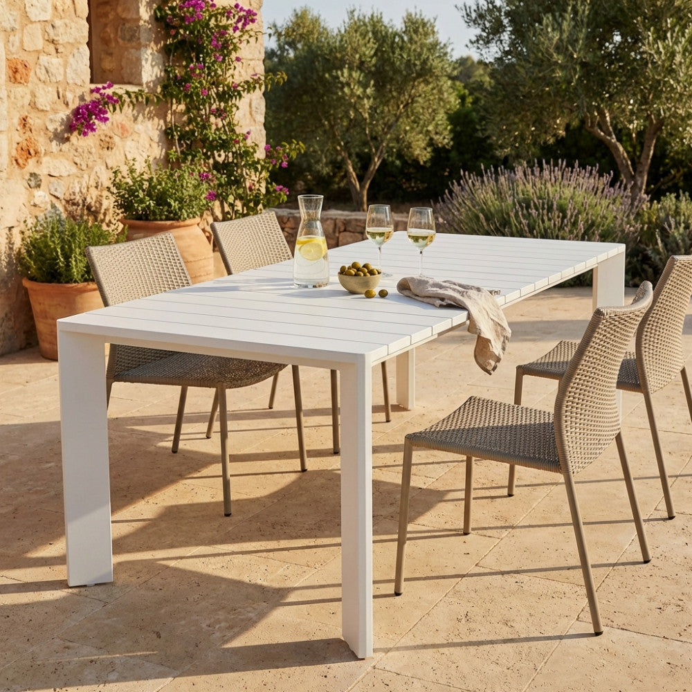 Tavolo da giardino Connecticut in alluminio bianco allestito su un patio in pietra con sedute in corda intrecciata e calici di vino.