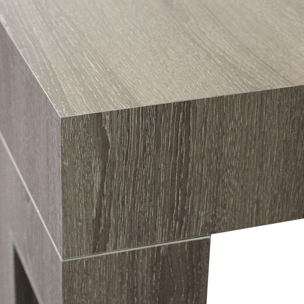 Dettaglio ravvicinato dell'angolo del tavolo in melaminico finitura taupe effetto legno.
