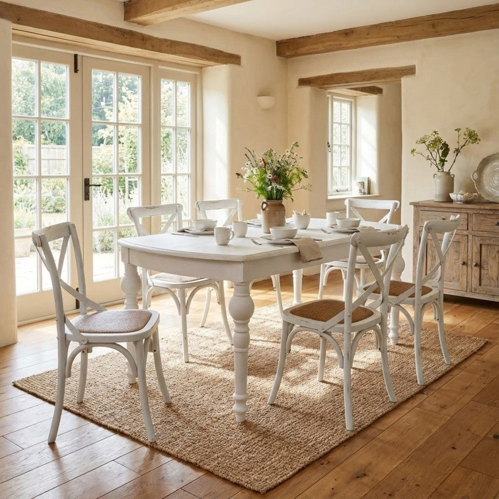 Sala da pranzo luminosa con il tavolo estensibile in legno bianco circondato da sedie incrociate abbinate su un tappeto in iuta.