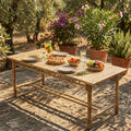 Tavolo da giardino Cuba Libre in legno allestito per un pasto all'aperto con frutta e bevande sotto la luce del sole.